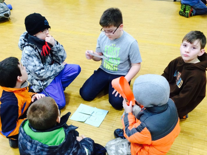 Students work in multi-age groups to assemble a falcon puzzle that helps them review school-wide expectations as part of a whole-school assembly in early January.